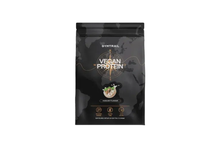 Ein schwarzer Beutel mit der Aufschrift Gymtrail Vegan Protein mit einer Weltkarte im Hintergrund und einer Kompassgrafik. Der Beutel zeigt eine Schale mit Haselnüssen, die auf den Haselnussgeschmack hinweist, sowie Symbole für Protein, Vitamine und Mineralstoffe.