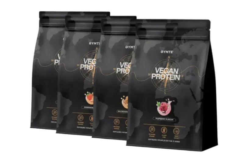 Vier schwarze Beutel mit veganem Proteinpulver sind in einer Reihe ausgestellt, die jeweils mit verschiedenen Geschmacksrichtungen und goldenen Akzenten versehen sind. Auf der Verpackung stehen der Markenname 